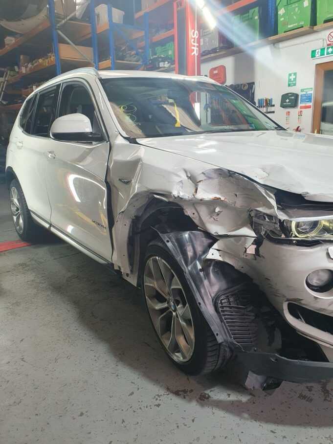 Front-end damaged white BMW SUV inside a car breakers dismantling facility Front-end damaged white BMW SUV inside a car breakers dismantling facility